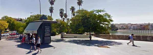 Un Kiosco con publicidad y personas junto al puente de Triana en Sevilla
